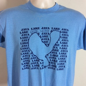 Può includere: Una maglietta blu chiaro con un contorno di un lago blu scuro. Il contorno è composto dalle parole "Java Lake" ripetute più volte.