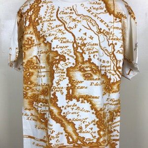 May include: White t-shirt with a brown vintage map print of Southeast Asia. The map includes the text "SIAM", "CAMBO", "OCHINCHIY", "Luthia", "Odil Siam", "Sornam", "Liam", "Plan Langy", "Mirim", "Lena Cerim", "Dinca", "P. de Patane", "Lorane", "Selen", "Malacca", "Andra", "11bo", "Praman", "Toda", and "C. Sem".