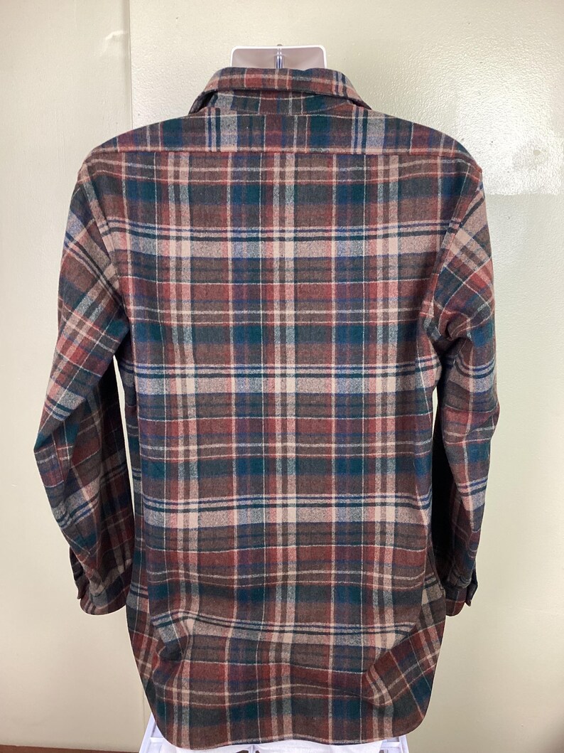 May include: A long-sleeved plaid shirt in brown, green, and beige tones. The shirt has a button-down collar and a relaxed fit.