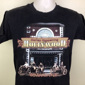 May include: Black t-shirt with a graphic print of a vintage movie theater with the text "Harley Happening of the HOLLYWOOD" and "GOWANDA, N.Y.".  The graphic also features five people riding motorcycles in front of the theater.