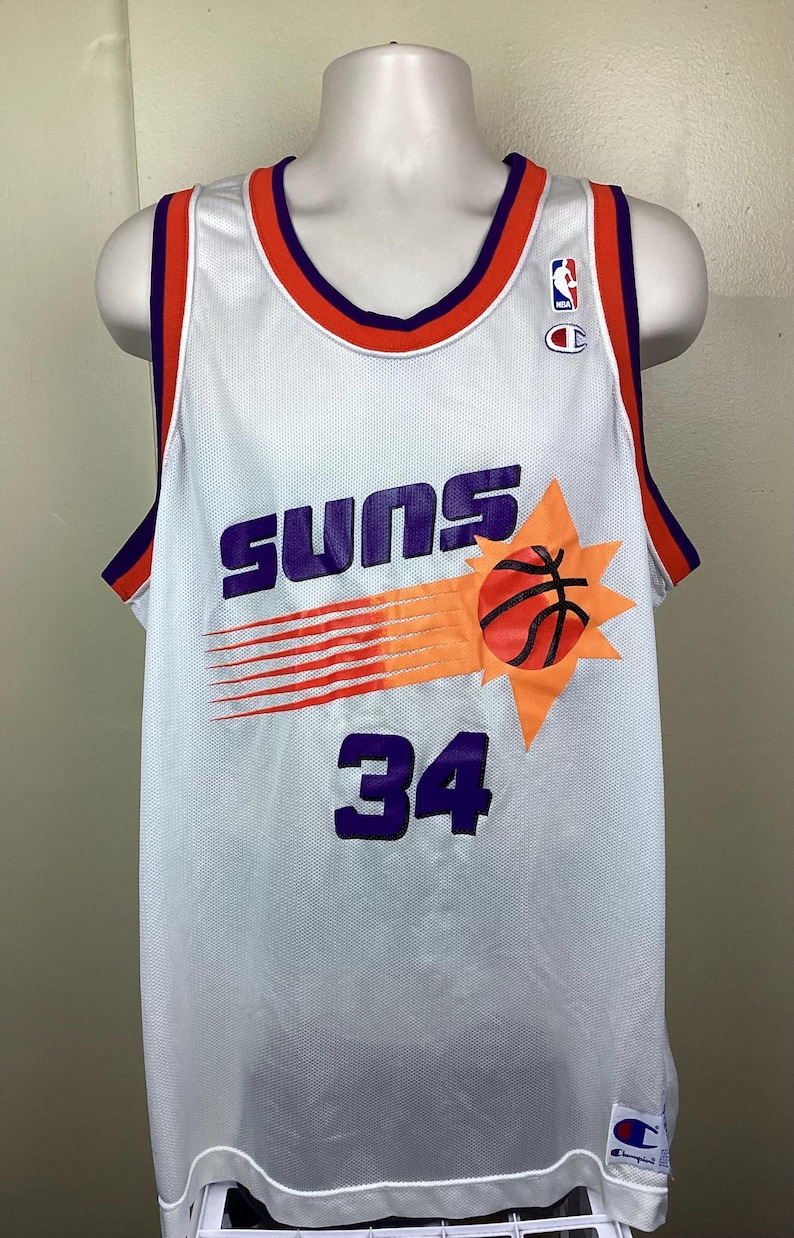 May include: White mesh basketball jersey with purple "SUNS" text, a basketball graphic, and the number 34 in purple. The jersey has orange and purple trim and a Champion logo.