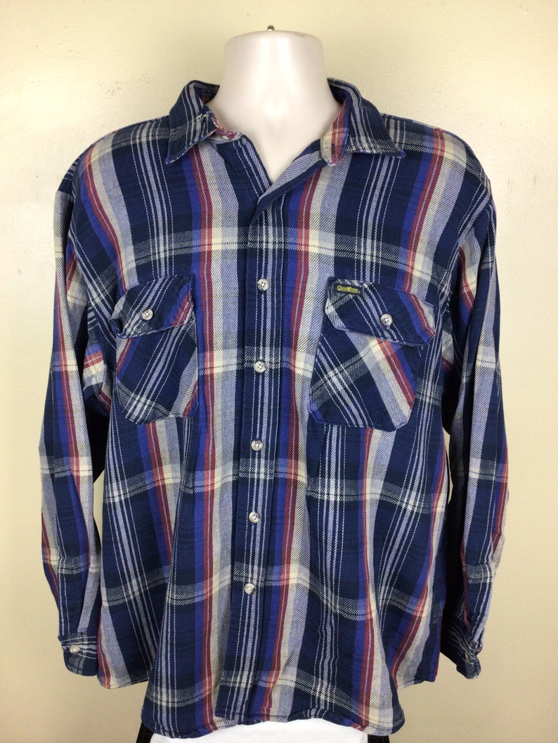 May include: A blue, red and white plaid long-sleeved button-down shirt with two chest pockets. The shirt has the brand name "Duck Head" on the right pocket.