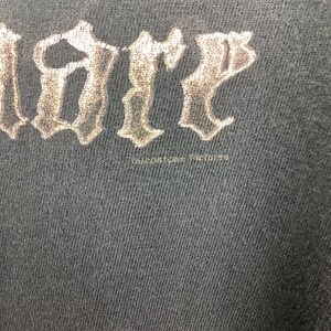 May include: Close-up of a dark gray t-shirt with the word "LIBER" in a stylized, metallic font. The text is slightly distressed, suggesting a vintage or worn appearance. The fabric has a subtle texture.