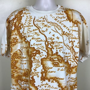 Può includere: Maglietta bianca con una stampa di mappa vintage marrone del sud-est asiatico. La mappa include il testo "Siam", "Camb", "Luthia", "Odje", "C. de las Res", "Martaban", "Plan", "Sornam", "Lena cerim", "Dinca", "Maon", "Peara", "Patani", "Pul", "Fanyon", "C. Sem", "Carst", "sonbila", "P. de", "Lag", "Da", "dos".