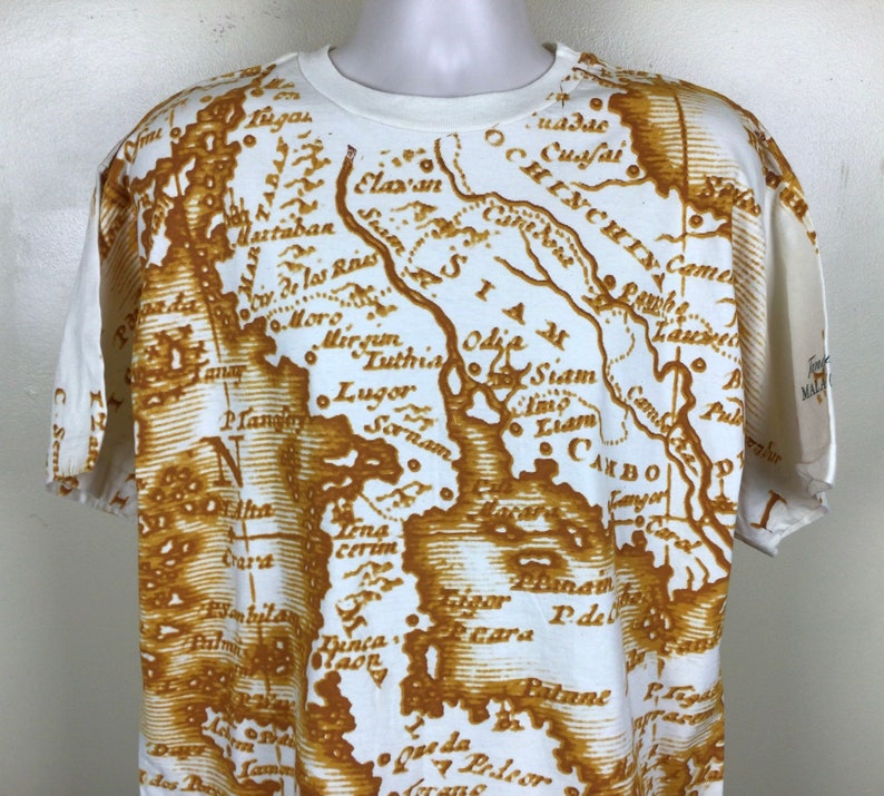 May include: White t-shirt with a brown vintage map print of Southeast Asia. The map includes the text "Siam", "Camb", "Luthia", "Odje", "C. de las Res", "Martaban", "Plan", "Sornam", "Lena cerim", "Dinca", "Maon", "Peara", "Patani", "Pul", "Fanyon", "C. Sem", "Carst", "sonbila", "P. de", "Lag", "Da", "dos".