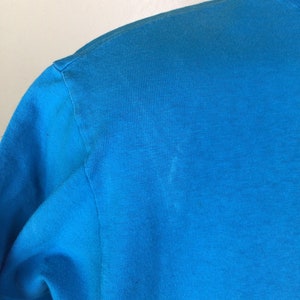 K&ouml;nnte beinhalten: Nahaufnahme eines leuchtend blauen T-Shirts. Der Stoff ist glatt und hat einen leichten Glanz.