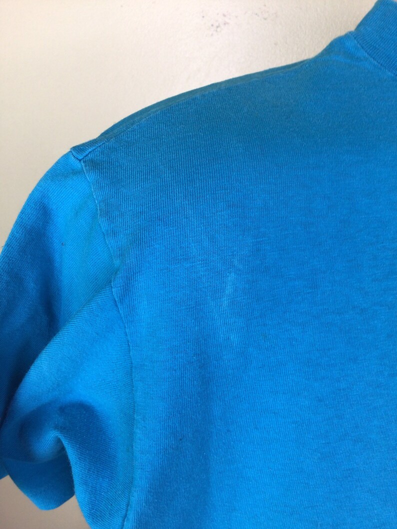 K&ouml;nnte beinhalten: Nahaufnahme eines leuchtend blauen T-Shirts. Der Stoff ist glatt und hat einen leichten Glanz.