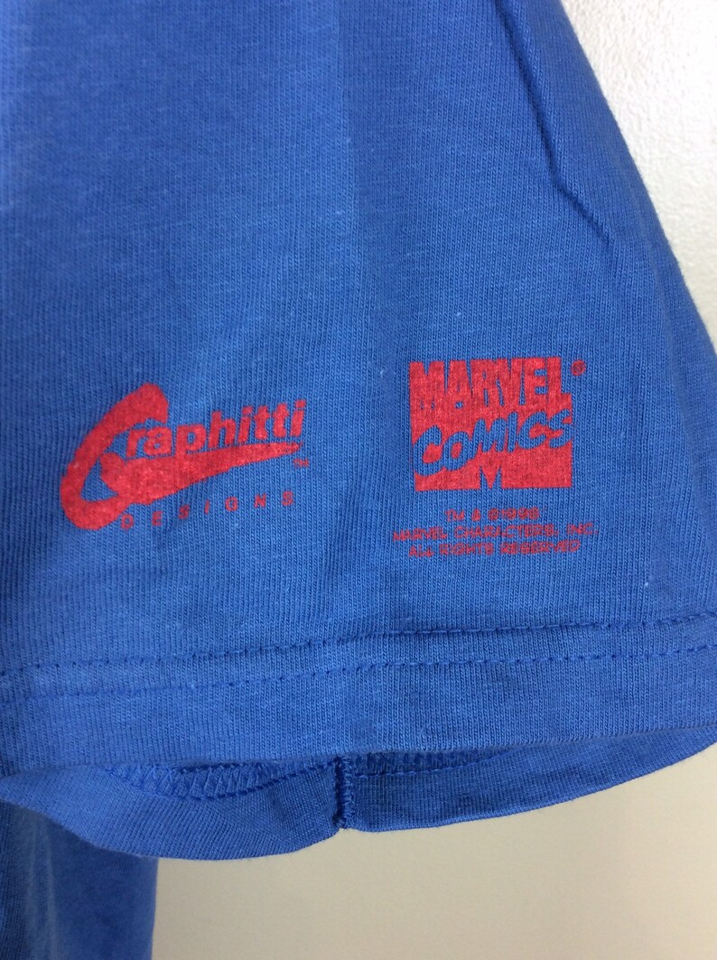 May include: A blue t-shirt with red text. The text reads "Graffiti Designs" and "Marvel Comics TM & &copy; 2003 Marvel Characters, Inc. All Rights Reserved."