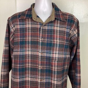 May include: A long-sleeved plaid shirt with a brown, red, green, and white plaid pattern. The shirt has a button-down collar and a button-up front.