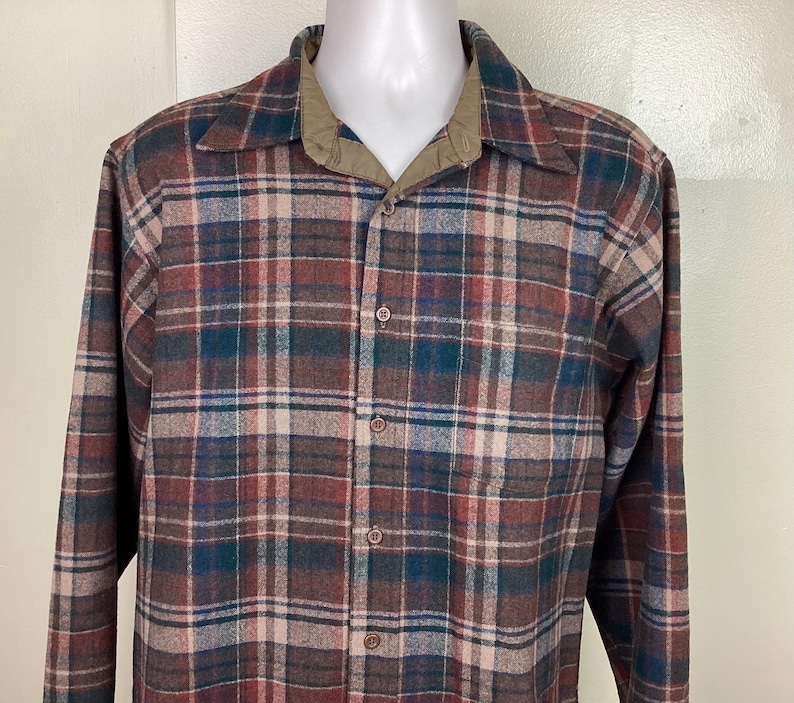 May include: A long-sleeved plaid shirt with a brown, red, green, and white plaid pattern. The shirt has a button-down collar and a button-up front.