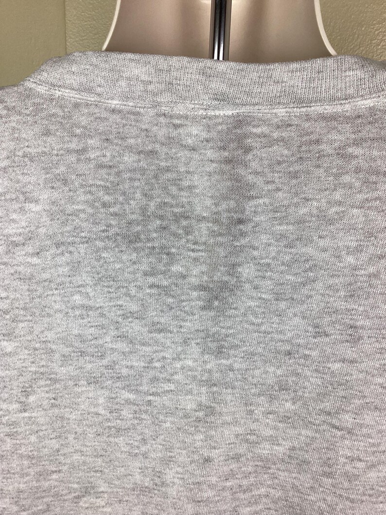 May include: Close-up of a gray collared shirt. The shirt is made of a soft, textured fabric. The collar is a lighter shade of gray than the body of the shirt.