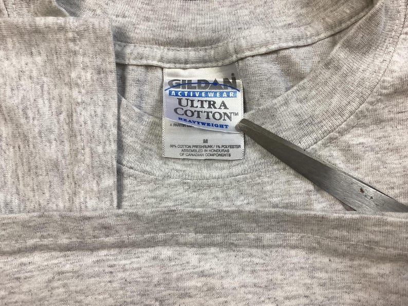 May include: A gray Gildan Ultra Cotton Heavyweight t-shirt tag with the text "Gildan Activewear Ultra Cotton Heavyweight" and "M" for size. The tag is made of white fabric with black text.