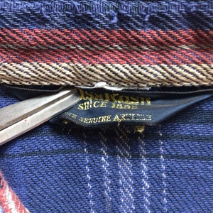 May include: Close-up of a blue and black plaid fabric with a black label that reads "Since 1883 Genuine Article".