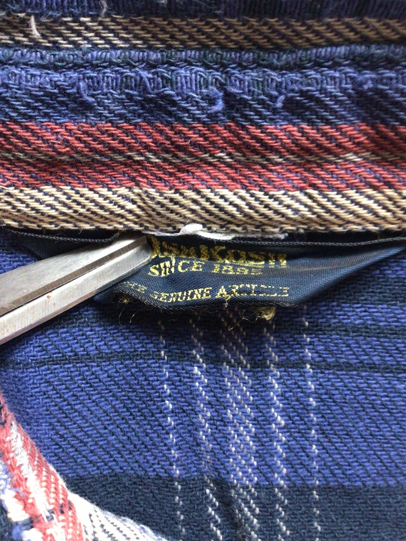 May include: Close-up of a blue and black plaid fabric with a black label that reads "Since 1883 Genuine Article".