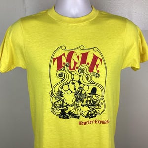 May include: Yellow t-shirt with a graphic design featuring the text "TGIF" in red, and a black and white illustration of figures playing instruments. The text "Courier-Express" is printed below the graphic.
