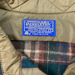 May include: A blue label with white text that reads "WARRANTED TO BE A PENDLETON" and "TRADE MARK REG. U.S. PAT. OFF. PENDLETON WOOLEN MILLS PORTLAND, OREGON 100% VIRGIN WOOL L PURE VIRGIN WOOL MADE IN U.S.A."