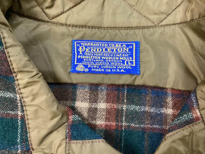 May include: A blue label with white text that reads "WARRANTED TO BE A PENDLETON" and "TRADE MARK REG. U.S. PAT. OFF. PENDLETON WOOLEN MILLS PORTLAND, OREGON 100% VIRGIN WOOL L PURE VIRGIN WOOL MADE IN U.S.A."