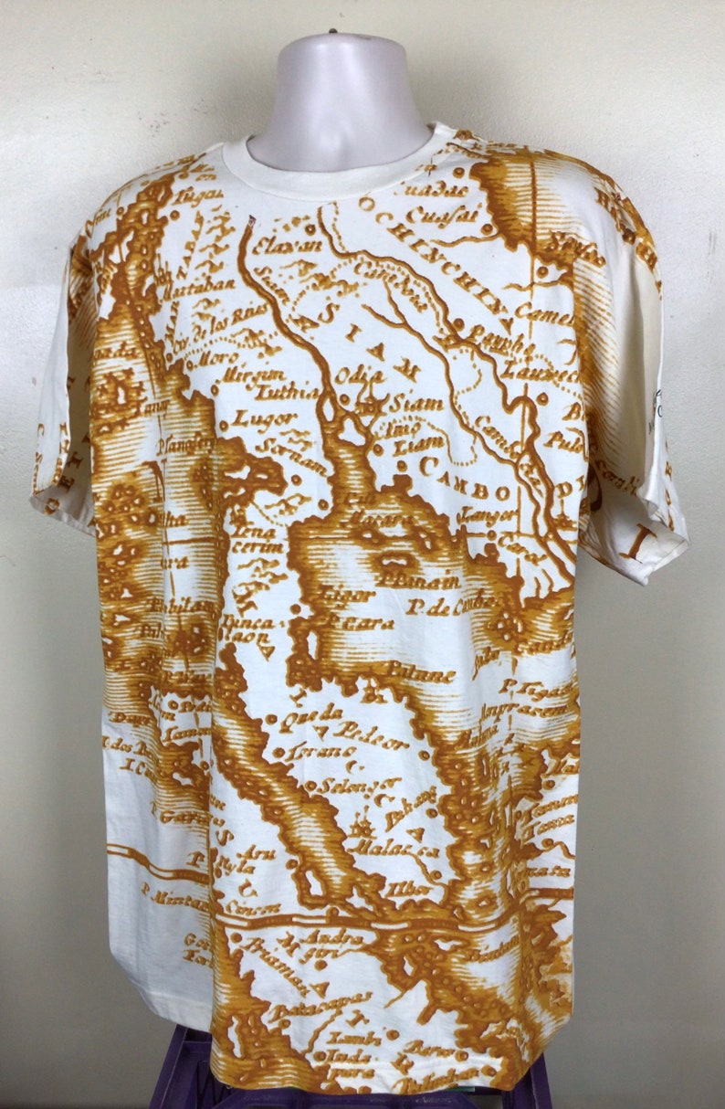 May include: White t-shirt with a vintage-style map print in brown. The map features various locations and names, including Siam, Odia, and Cambo.