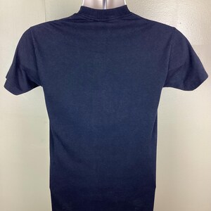 Pu&ograve; includere: T-shirt nero tinta unita a maniche corte, presentato su un manichino. La maglietta ha un girocollo e un design semplice e classico. Il tessuto sembra essere un morbido misto cotone, adatto per abbigliamento casual.