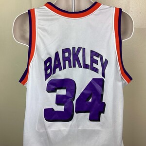 May include: White basketball jersey with the name "BARKLEY" and the number "34" in purple. The jersey has orange and purple trim around the neck and arm openings. The jersey is displayed on a mannequin.
