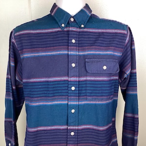 May include: A button-down shirt with horizontal stripes in shades of blue, teal, and purple. The long-sleeved shirt has a button-down collar and a single chest pocket. The shirt is displayed on a white mannequin.