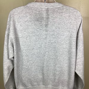 May include: A heather gray sweatshirt with a crew neck and long sleeves. The sweatshirt is displayed on a mannequin. The fabric appears to be a soft, comfortable material, suitable for casual wear. The overall design is simple and classic.