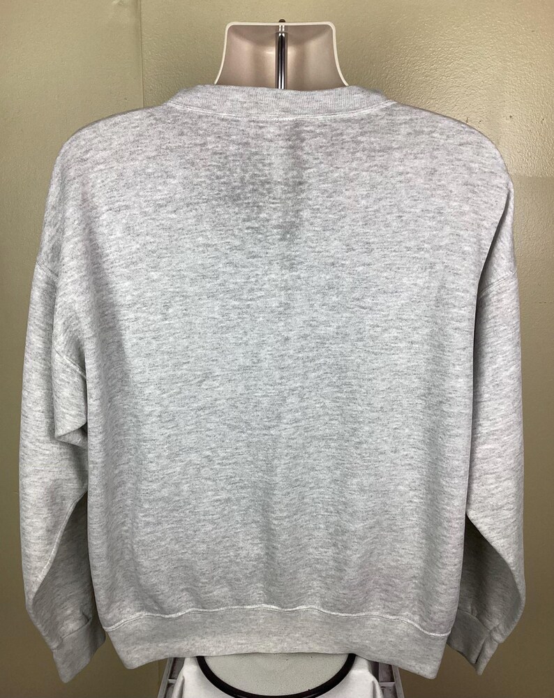 May include: A heather gray sweatshirt with a crew neck and long sleeves. The sweatshirt is displayed on a mannequin. The fabric appears to be a soft, comfortable material, suitable for casual wear. The overall design is simple and classic.