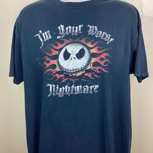 May include: Dark blue t-shirt featuring a graphic of Jack Skellington's face surrounded by flames. The text "I'm your Worst Nightmare" is above and below the image in a gothic font. The shirt is displayed on a mannequin.