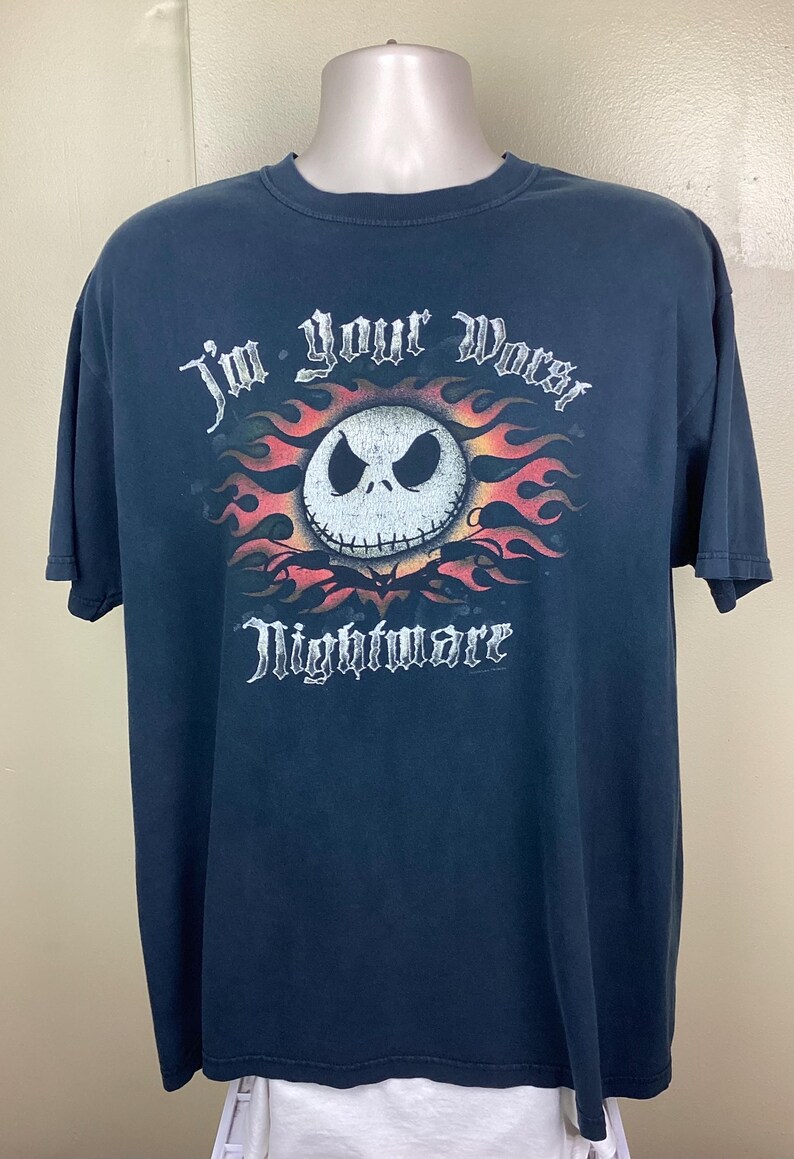May include: Dark blue t-shirt featuring a graphic of Jack Skellington's face surrounded by flames. The text "I'm your Worst Nightmare" is above and below the image in a gothic font. The shirt is displayed on a mannequin.