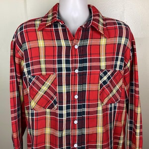 May include: Red plaid button-up shirt with yellow, navy, and white accents. The shirt has two front pockets and white buttons. The long-sleeved shirt is displayed on a mannequin.