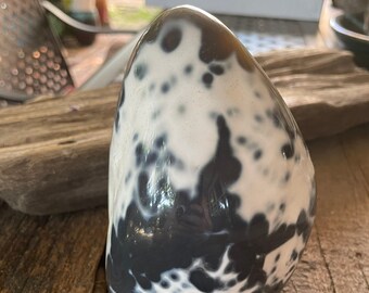 May include: A smooth, polished, black and white agate stone with a speckled pattern. The stone is shaped like an egg and has a glossy finish.