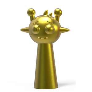 May include: A golden-colored figurine with a stylized alien-like design. The figure has a round head with large eyes, small antennae, and a smiling mouth. The body is a tapered cone shape, giving it a whimsical appearance.
