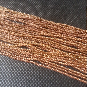 Peut inclure: Gros plan de plusieurs brins de chaîne de couleur cuivre. Les chaînes sont étroitement tissées, créant une surface texturée. Les chaînes sont disposées en diagonale sur un fond sombre et texturé.