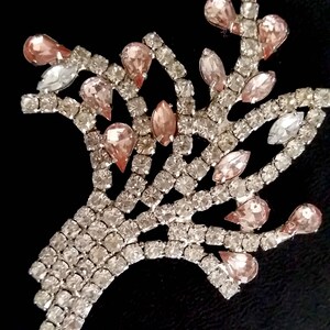 May include: A silver and pink rhinestone brooch shaped like a tree with a delicate design. The brooch is made of small, sparkling rhinestones.