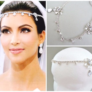 May include: Silver bridal headpiece with a delicate chain and dangling crystals. The headpiece features a floral design with a teardrop crystal accent.
