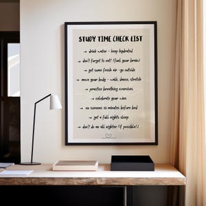 Puede incluir: Un marco negro muestra una "Study Time Check List" en fuente manuscrita negra. La lista incluye consejos como beber agua, comer y tomar aire fresco. La impresión está sobre un escritorio con una lámpara y otros objetos.