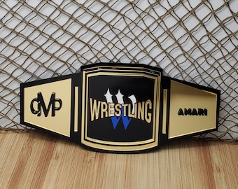 May include: A black wrestling championship belt with gold accents. The belt has the word "WRESTLING" in white letters with a blue "W" in the center. The belt also has the names "CMP" and "AMARI" on the sides.
