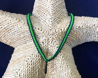 May include: A black and green lanyard with a small black charm. The lanyard is displayed on a woven starfish.