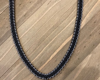 May include: A black and white paracord lanyard with a black metal clip. The lanyard is made of braided cord and has a white stripe running down the center.