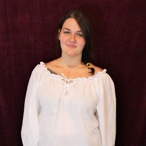 May include: A white peasant blouse with a ruffled neckline and long sleeves. The blouse is tied at the neck with a string. The model is wearing a black skirt.