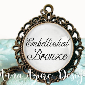 May include: A bronze pendant with an ornate design and a white glass cameo featuring the text "Embellished Bronze".