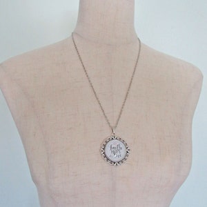 May include: Silver chain necklace with a round pendant featuring a white background and the words "Faith Hope Love" in black script.