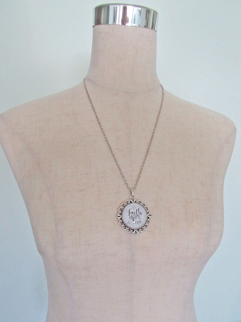 May include: Silver chain necklace with a round pendant featuring a white background and the words "Faith Hope Love" in black script.