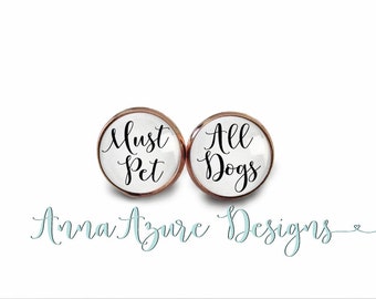 May include: A pair of rose gold earrings with white glass cabochons. The left earring says "Must Pet" and the right earring says "All Dogs".