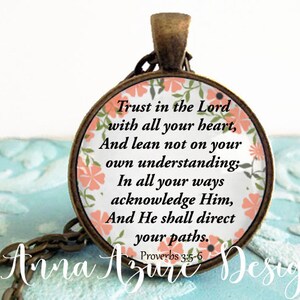 May include: A round pendant necklace with a floral design and the text "Trust in the Lord with all your heart, And lean not on your own understanding; In all your ways acknowledge Him, And He shall direct your paths. Proverbs 3:5-6"