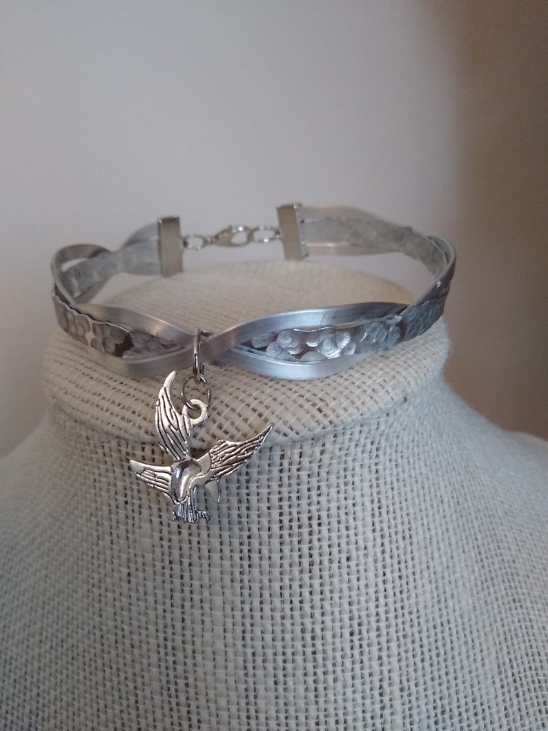 May include: A silver metal choker necklace with a braided design and a silver bird charm.