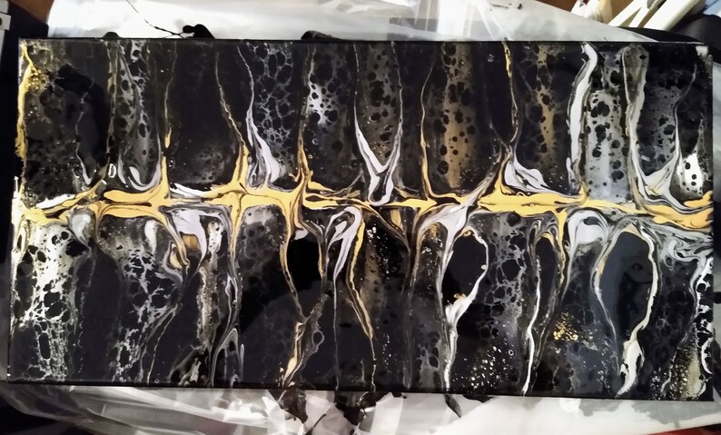 May include: Abstract art painting with black, white, and gold paint. The paint is swirled and layered to create a unique design. The painting is on a canvas.