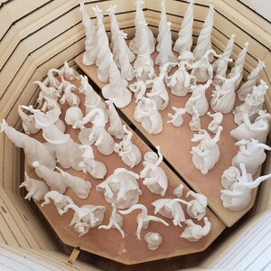 K&ouml;nnte beinhalten: Eine Sammlung wei&szlig;er Keramikfiguren, darunter Weihnachtsb&auml;ume und skurrile, zwergenartige Figuren, die in einem Ofen angeordnet sind. Die Figuren sind in verschiedenen Posen und Gr&ouml;&szlig;en, bereit zum Brennen.