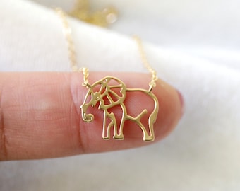 Può includere: Una collana con ciondolo a forma di elefante dorato. Il design dell'elefante è un contorno minimalista con orecchie dettagliate. La collana è su una catena delicata e lo sfondo è un tessuto bianco morbido.