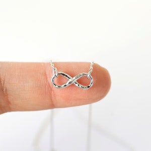 May include: A delicate silver necklace featuring an infinity symbol pendant. The pendant is textured and hangs from a fine chain. The necklace is displayed against a white background.